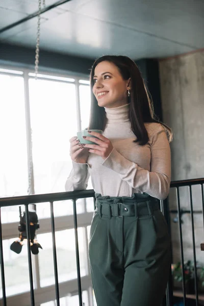 Mujer sonriente de pie en el balcón con capuchino en la cafetería - foto de stock