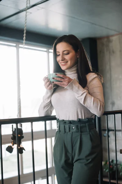 Mujer sonriente de pie en el balcón con capuchino en la cafetería - foto de stock