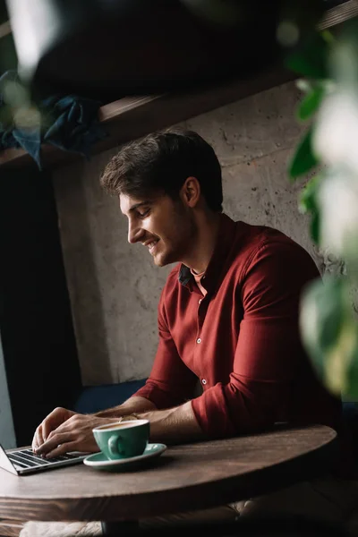 Sorrindo jovem freelancer trabalhando no laptop no café — Fotografia de Stock