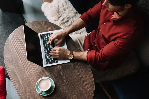 Vista aérea del joven freelancer que trabaja en la computadora portátil en la cafetería - foto de stock