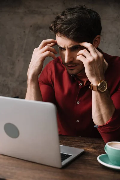 Pensativo joven freelancer trabajando en el ordenador portátil y beber café en la cafetería - foto de stock