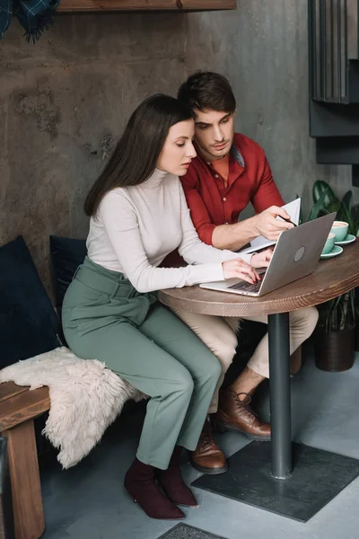 Pareja joven que trabaja en el ordenador portátil en la cafetería moderna - foto de stock