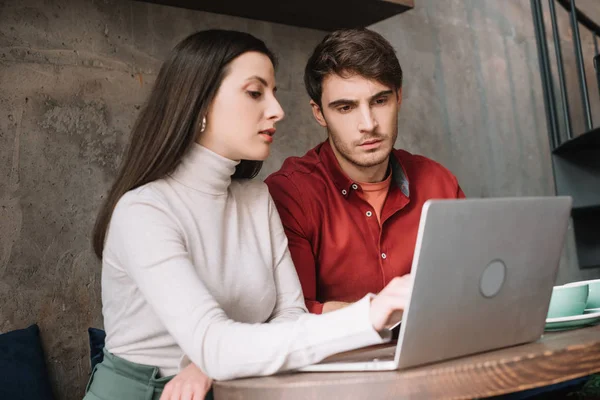 Pareja joven trabajando juntos en el ordenador portátil en la cafetería - foto de stock