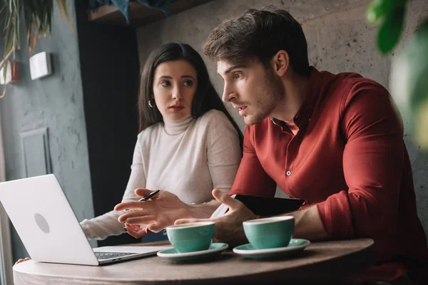 Pareja joven hablando y trabajando en el ordenador portátil en la cafetería - foto de stock