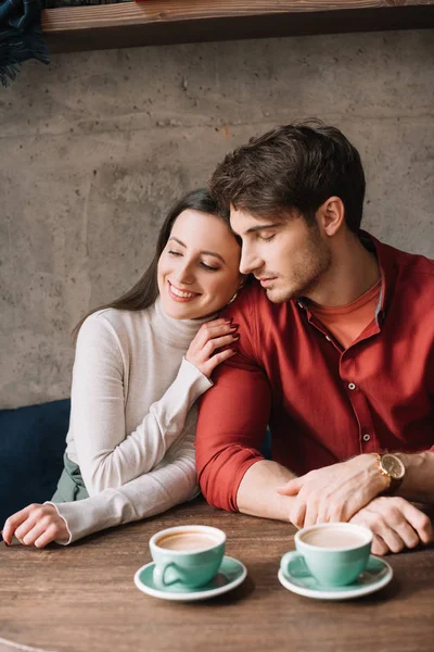 Sourire tendre jeune couple étreignant et buvant du café dans un café — Photo de stock