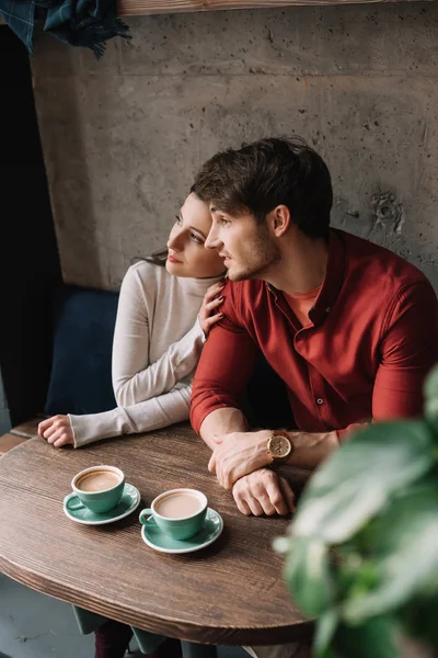 Selective focus of green leaves and romantic young couple hugging and drinking coffee in coffee shop — Stock Photo