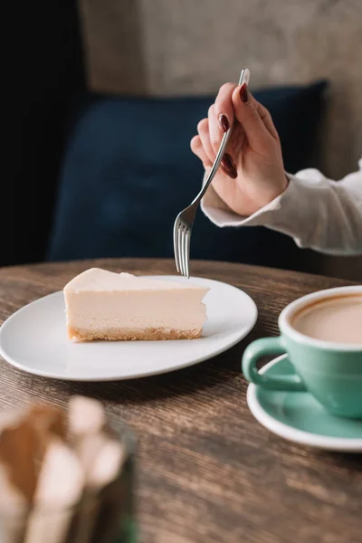 Vista cortada de mulher comer cheesecake com garfo e beber café no café — Fotografia de Stock