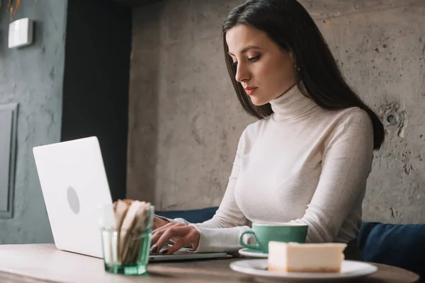 Freelancer using laptop near coffee and cheesecake in coffee shop — Stock Photo