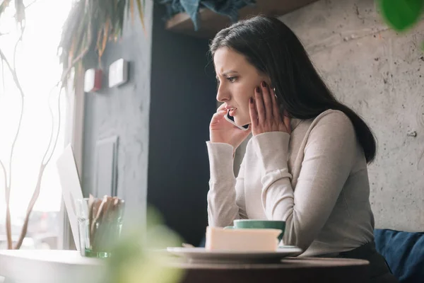 Foyer sélectif de plantes vertes et freelance bouleversé en utilisant un ordinateur portable et parler sur smartphone dans un café — Photo de stock