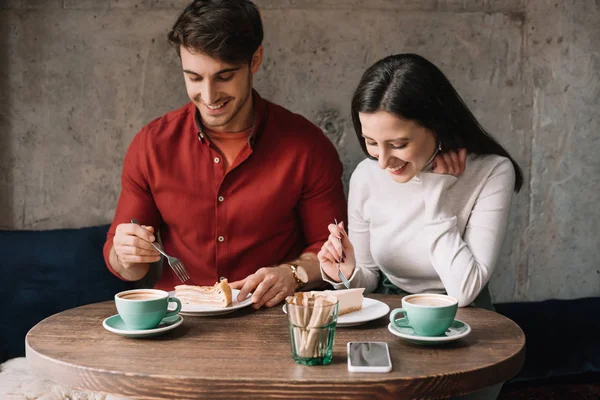 Feliz pareja comiendo pastel de queso y beber capuchino en la cafetería - foto de stock