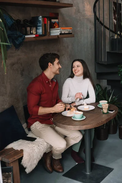 Casal feliz comendo cheesecake, bebendo cappuccino e olhando um para o outro no café — Fotografia de Stock