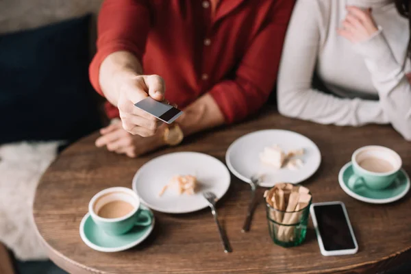 Cropped view of young couple eating cheesecake and drinking coffee while man holding credit card in coffee shop — Stock Photo