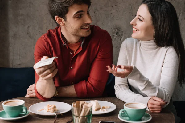 Happy couple looking at each other while man holding money in coffee shop — Stock Photo