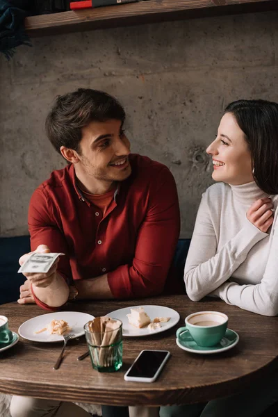 Щаслива пара дивиться один на одного, а чоловік тримає гроші в кав'ярні — стокове фото