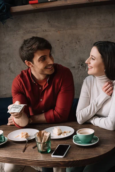 Coppia felice guardando l'un l'altro, mentre l'uomo in possesso di soldi in caffetteria — Foto stock