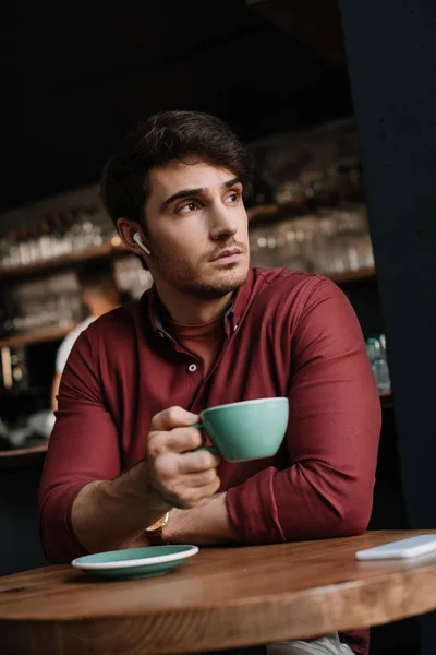 Dreamy man in wireless earphones drinking coffee coffee in cafe — Stock Photo