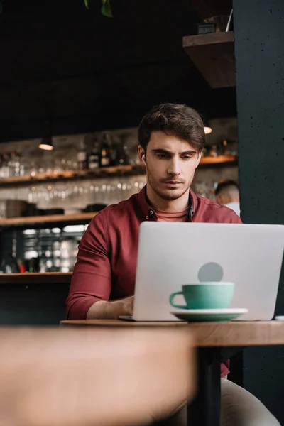 Freelancer em fones de ouvido sem fio usando laptop em cafetaria — Fotografia de Stock