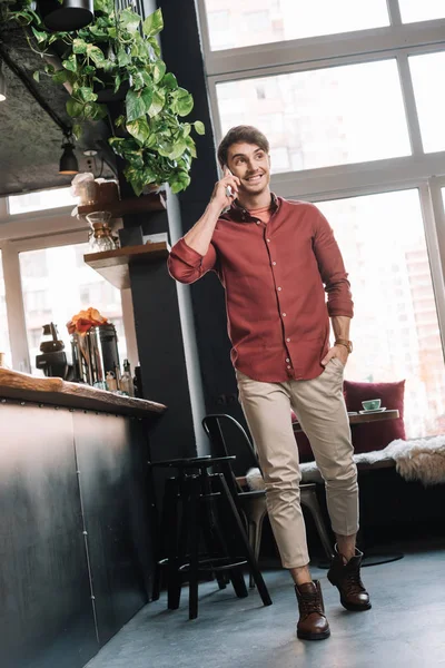 Smiling handsome man walking near bar counter and talking on smartphone — Stock Photo