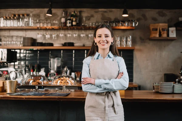 Barista souriant dans tablier debout avec les bras croisés près comptoir bar — Photo de stock