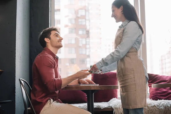 Camarera sonriente que sirve café al hombre con portátil - foto de stock