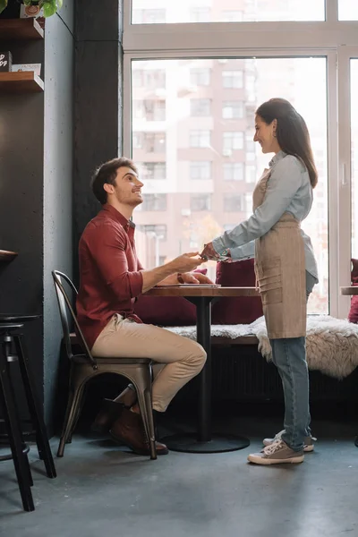 Camarera sonriente que sirve café al hombre con portátil - foto de stock