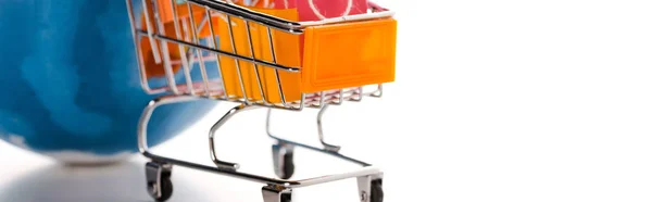 Plano panorámico de carrito de compras de juguete con bolsas de compras cerca del mundo en blanco, concepto de comercio electrónico - foto de stock
