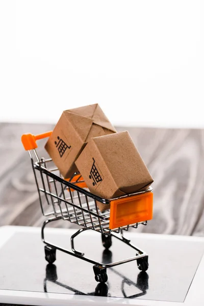 Carrito de compras de juguete con cajas pequeñas en tableta digital aislada en blanco, concepto de comercio electrónico - foto de stock