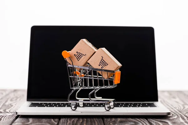 Toy shopping cart with small carton boxes on laptop with blank screen isolated on white, e-commerce concept — Stock Photo