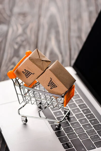 Foco seletivo de caixas de papelão de brinquedo no carrinho de compras pequeno no laptop com tela em branco, conceito de e-commerce — Fotografia de Stock