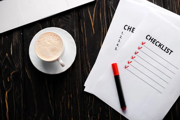 Vista superior de los papeles con lista de verificación y rotulador rojo cerca de la taza de café en la mesa - foto de stock