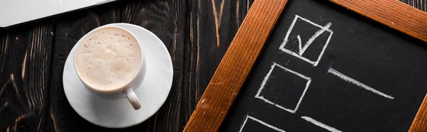Tiro panorâmico de tábua de giz com checklist perto de xícara de café na mesa — Fotografia de Stock