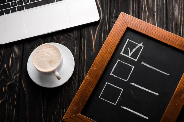 Vista dall'alto del pannello di gesso con checklist vicino a tazza di caffè e laptop sul tavolo, concetto di e-commerce — Foto stock