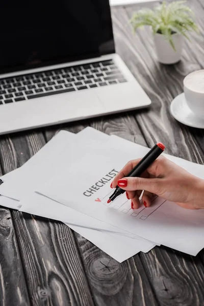 Vista cortada de empresária segurando caneta marcador vermelho perto da lista de verificação, copo e laptop na mesa, conceito de e-commerce — Fotografia de Stock