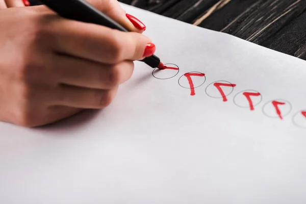 Cropped view of woman holding marker pen near red ticks on paper — Stock Photo