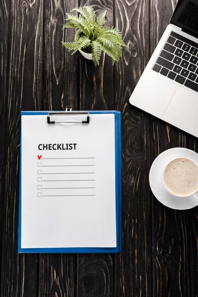 Vue du haut du presse-papiers avec check-list près de l'ordinateur portable, plante, stylo marqueur rouge et tasse de café sur la table, concept de commerce électronique — Photo de stock