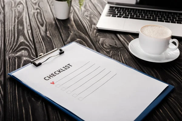 Foyer sélectif de presse-papiers avec check-list près de l'ordinateur portable et tasse de café sur la table, concept e-commerce — Photo de stock