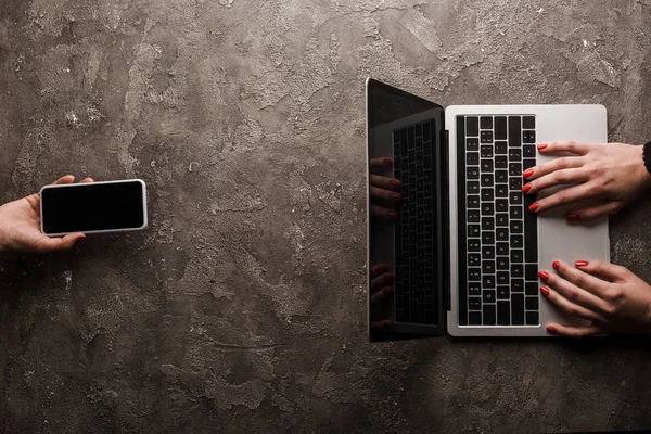 Top view of businesswoman holding smartphone with blank screen near colleague typing laptop, e-commerce concept — Stock Photo