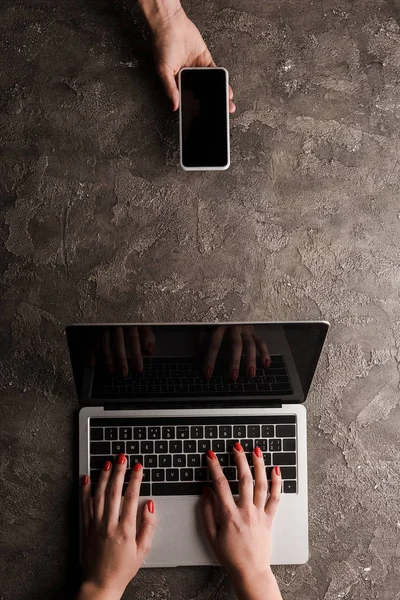 Вид сверху на деловую женщину, держащую смартфон с пустым экраном рядом с коллегой, печатающей на ноутбуке, концепция электронной коммерции — стоковое фото