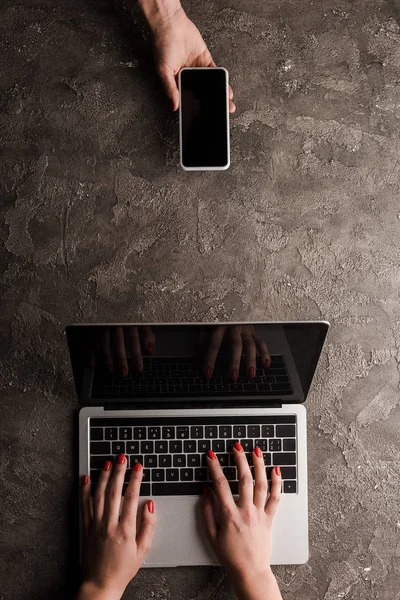 Vista superior de la mujer de negocios sosteniendo teléfono inteligente con pantalla en blanco cerca de compañeros de trabajo escribiendo en el ordenador portátil, concepto de comercio electrónico - foto de stock