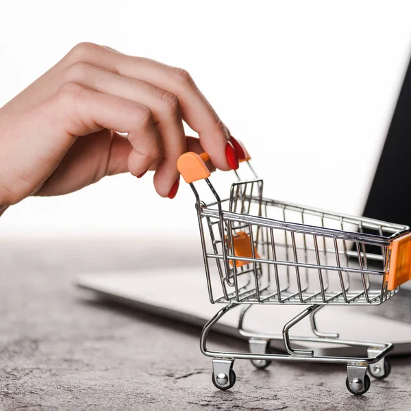 Close up of woman holding toy shopping cart near laptop isolated on white, e-commerce concept — Stock Photo