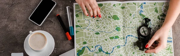 Panoramic shot of woman near map, compass, cup with coffee and gadgets — Stock Photo