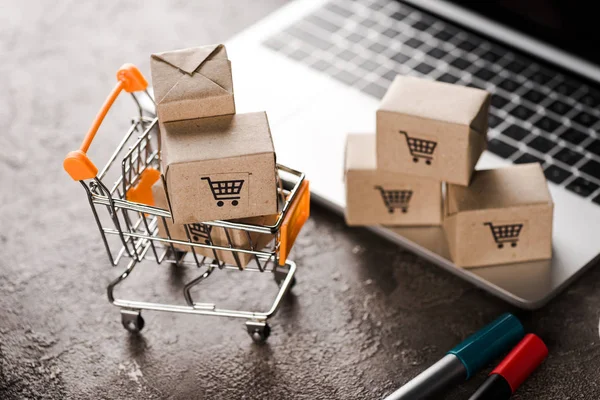 Selective focus of toy shopping cart with small carton boxes near laptop, e-commerce concept — Stock Photo