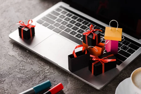 Enfoque selectivo de bolsas de compras cerca de la computadora portátil, taza de café y rotuladores, concepto de comercio electrónico - foto de stock