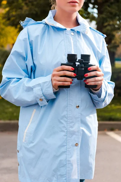 Cropped view of woman in blue raincoat holding binoculars — Stock Photo