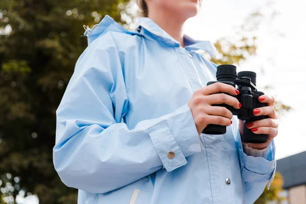 Vue recadrée de la femme en imperméable tenant des jumelles à l'extérieur — Photo de stock