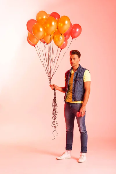 Schöner Mann mit orangefarbenen Luftballons auf rosa — Stockfoto