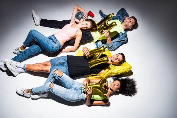 Top view of happy multicultural friends lying with festive balloons on white — Stock Photo