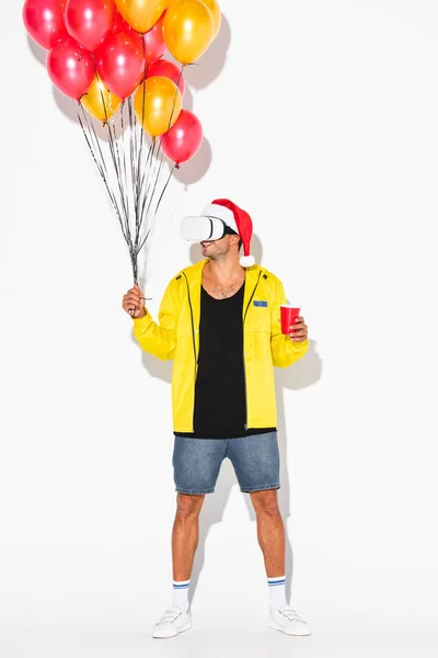 Fröhlicher Mann im Virtual-Reality-Headset mit Plastikbecher und Luftballons auf weißem Grund — Stockfoto