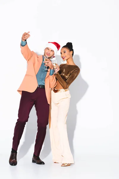 Happy man in santa hat talking selfie with attractive african american girl on white — Stock Photo