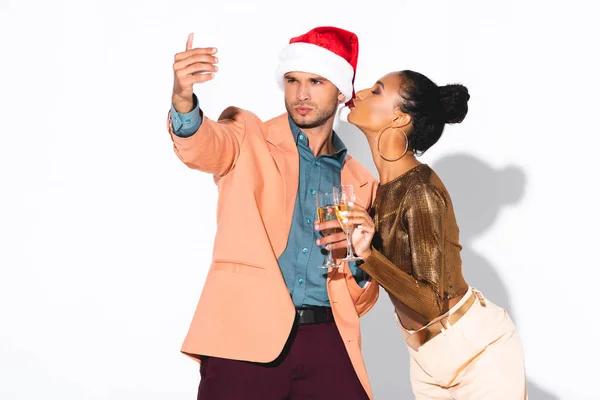 Handsome man in santa hat taking selfie near african american girl with duck face on white — Stock Photo